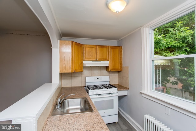 7152 N 20th St, Philadelphia, PA 19138 - kitchen featuring white gas range oven, under cabinet range hood, backsplash, radiator heating unit, and arched walkways