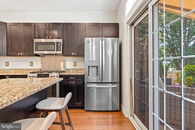 311 W 3rd Ave, Conshohocken, PA 19428 - kitchen featuring appliances with stainless steel finishes, dark brown cabinetry, light wood-type flooring, light stone counters, and a kitchen breakfast bar