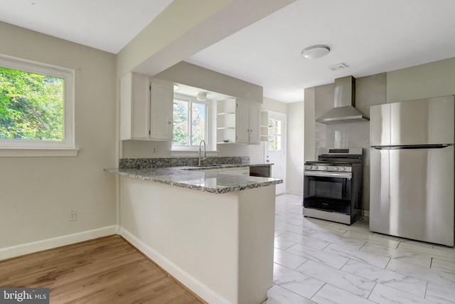 6005 Frederick St, Springfield, VA 22150 - kitchen featuring appliances with stainless steel finishes, wall chimney range hood, light stone countertops, a peninsula, and white cabinetry