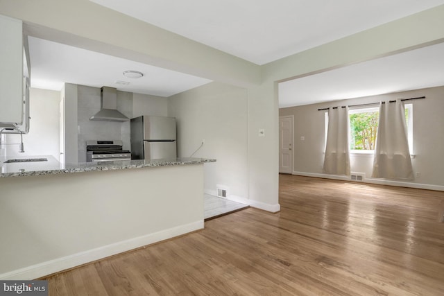 6005 Frederick St, Springfield, VA 22150 - kitchen with stainless steel appliances, wall chimney exhaust hood, light stone counters, light wood-style floors, and a peninsula