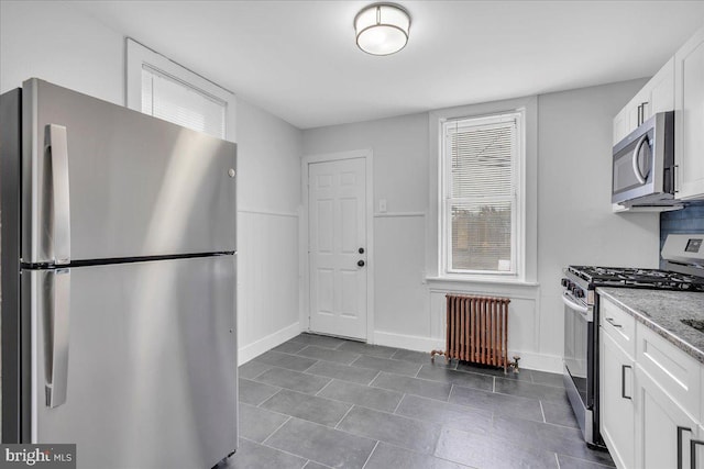1528 Park Blvd, Camden, NJ 08103 - kitchen with appliances with stainless steel finishes, radiator heating unit, white cabinetry, dark tile patterned flooring, and light stone countertops