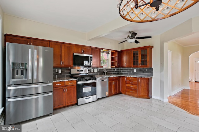 4713 Elsrode Ave, Baltimore, MD 21214 - kitchen featuring appliances with stainless steel finishes, backsplash, arched walkways, light stone counters, and glass insert cabinets