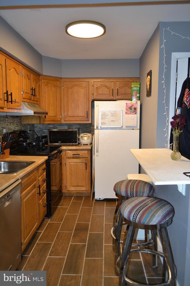 4701 Pennell Rd Unit A-6, Aston, PA 19014 - kitchen featuring appliances with stainless steel finishes, ventilation hood, tasteful backsplash, brown cabinetry, and light countertops