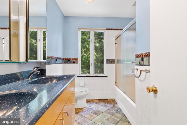 39 Haymarket Ln, Bryn Mawr, PA 19010 - full bath with tile walls, double vanity, bath / shower combo with glass door, wainscoting, and tile patterned floors