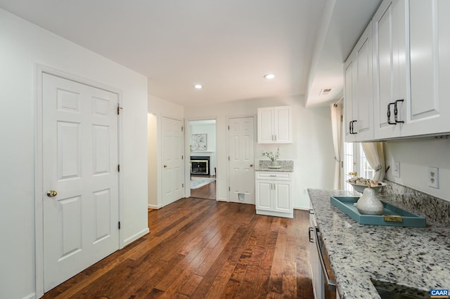 1632 Farm Brook Pl, Charlottesville, VA 22901 - kitchen featuring dark wood finished floors, white cabinets, light stone counters, a glass covered fireplace, and recessed lighting