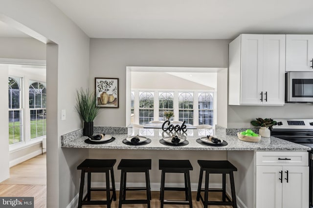 202 Piping Rock Dr, Silver Spring, MD 20905 - kitchen with appliances with stainless steel finishes, white cabinetry, light stone counters, a kitchen bar, and light wood-type flooring
