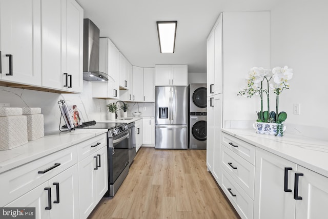 205 Yoakum Pkwy Unit 1712, Alexandria, VA 22304 - kitchen with appliances with stainless steel finishes, wall chimney exhaust hood, stacked washer and clothes dryer, light wood finished floors, and white cabinetry