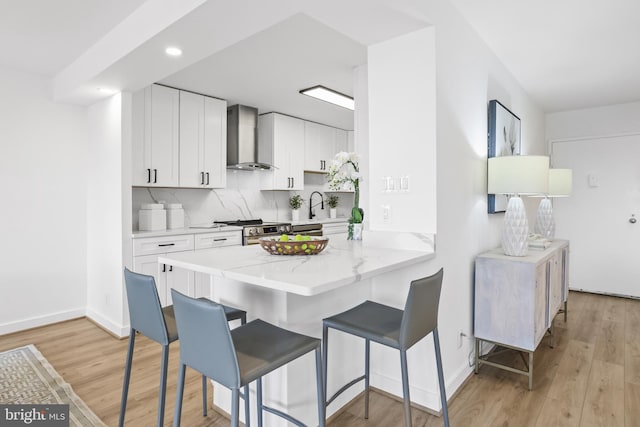205 Yoakum Pkwy Unit 1712, Alexandria, VA 22304 - kitchen featuring wall chimney range hood, light stone counters, a breakfast bar, light wood-style floors, and recessed lighting