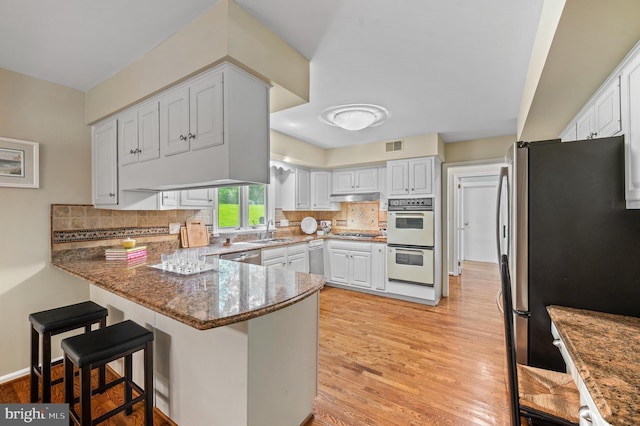 130 Hunt Valley Cir, Berwyn, PA 19312 - kitchen with stainless steel appliances, a peninsula, light wood-type flooring, and stone counters
