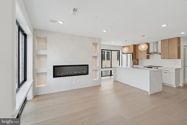 919 S 11th St Unit A, Philadelphia, PA 19147 - kitchen with wall chimney range hood, freestanding refrigerator, light wood-style floors, a glass covered fireplace, and light countertops