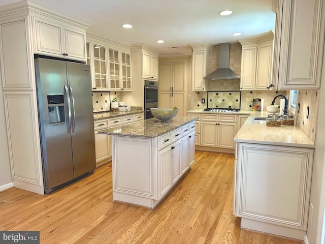1517 Tuba Ct, Vienna, VA 22182 - kitchen featuring appliances with stainless steel finishes, wall chimney range hood, a center island, light wood-type flooring, and decorative backsplash
