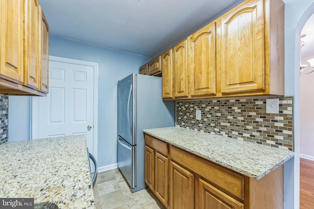 2864 Cushing Rd, Camden, NJ 08104 - kitchen featuring arched walkways, decorative backsplash, light stone counters, freestanding refrigerator, and brown cabinets