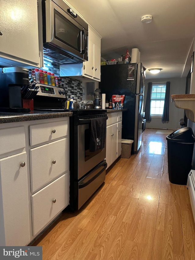 884 Main St, Pennsburg, PA 18073 - kitchen with appliances with stainless steel finishes, white cabinetry, dark countertops, light wood-style floors, and decorative backsplash