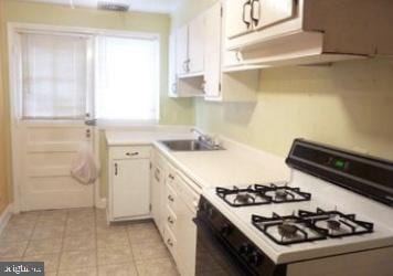 1527 Ingleside Ave, Baltimore, MD 21207 - kitchen with white range with gas cooktop, light countertops, white cabinetry, and light tile patterned floors