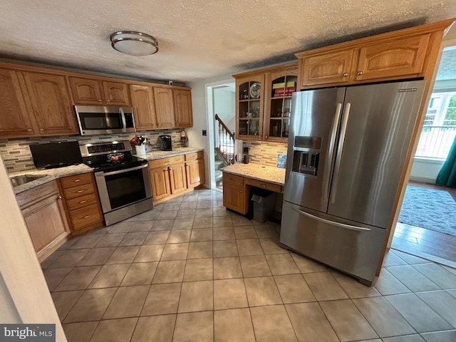 27 Dunlin Way, Sicklerville, NJ 08081 - kitchen with appliances with stainless steel finishes, backsplash, light tile patterned floors, glass insert cabinets, and light stone counters