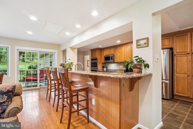 3010 Phyllmar Pl, Oakton, VA 22124 - kitchen with appliances with stainless steel finishes, light stone counters, brown cabinetry, a kitchen bar, and recessed lighting