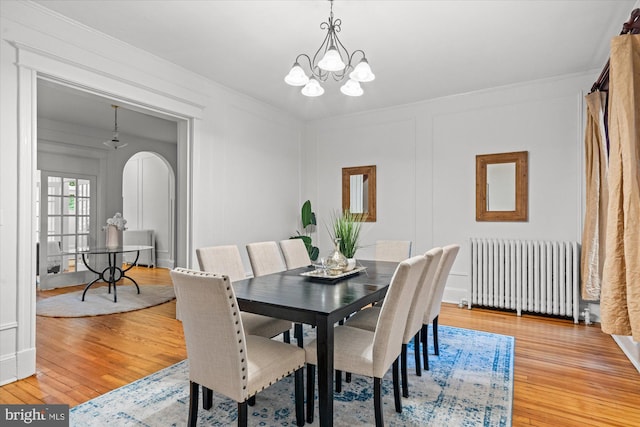 2637 Garfield St NW, Washington, DC 20008 - dining room featuring radiator heating unit, light wood-type flooring, a chandelier, arched walkways, and crown molding