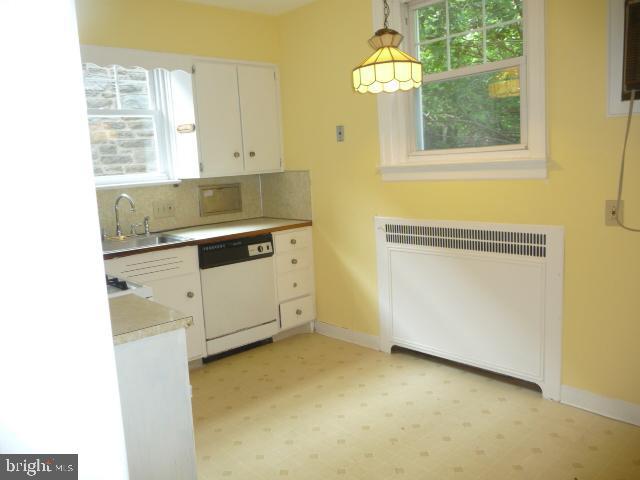537 E Comly St, Philadelphia, PA 19120 - kitchen with white dishwasher, radiator, plenty of natural light, and white cabinets