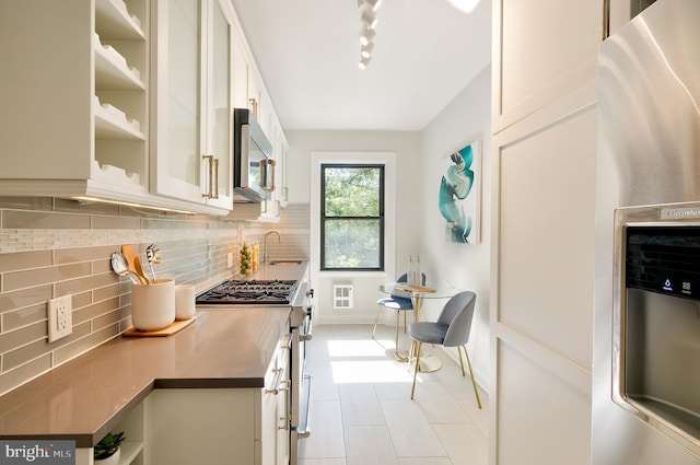 3100 Connecticut Ave NW Unit 434, Washington, DC 20008 - kitchen featuring appliances with stainless steel finishes, backsplash, light tile patterned floors, white cabinetry, and rail lighting
