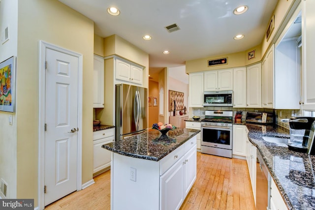 57 Harwood Rd, Monroe Township, NJ 08831 - kitchen featuring appliances with stainless steel finishes, a center island, light wood-type flooring, dark stone counters, and white cabinets