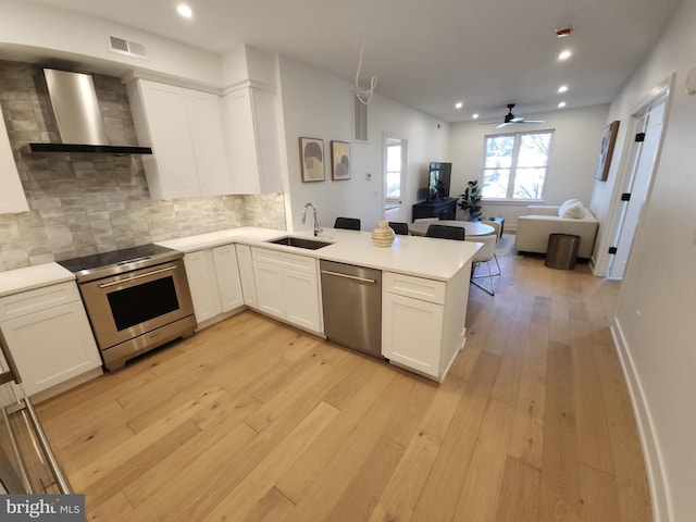 8610 Evergreen Pl Unit 100, Philadelphia, PA 19118 - kitchen with stainless steel appliances, wall chimney exhaust hood, a peninsula, tasteful backsplash, and white cabinetry