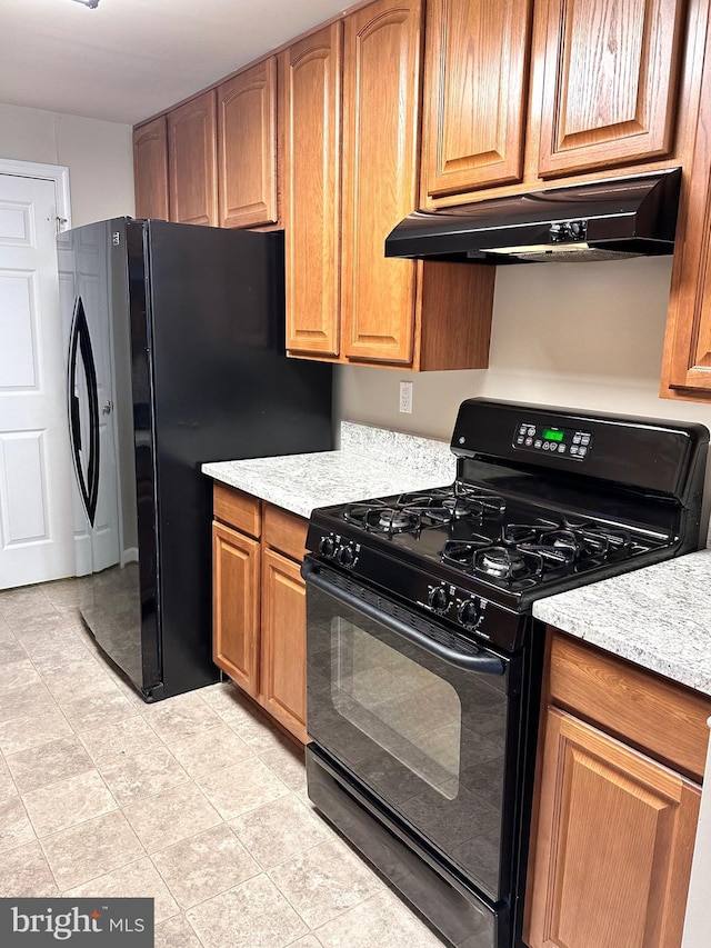 8980 Harrover Pl Unit 80B, Lorton, VA 22079 - kitchen featuring black range with gas stovetop, under cabinet range hood, light tile patterned floors, brown cabinets, and freestanding refrigerator