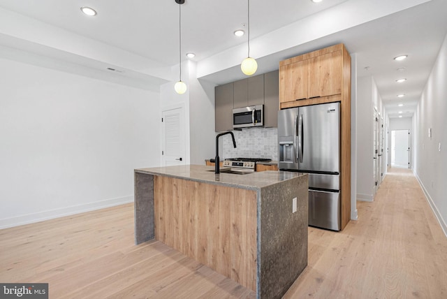 1338 N Franklin St, Philadelphia, PA 19122 - kitchen featuring appliances with stainless steel finishes, light wood-type flooring, tasteful backsplash, dark stone countertops, and a kitchen island with sink