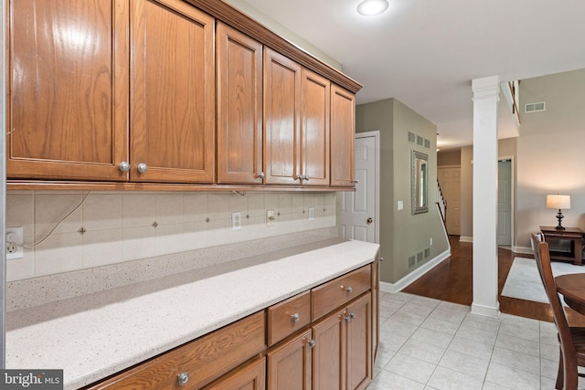 16 Fox Hollow Dr, Lancaster, PA 17602 - kitchen with light tile patterned flooring, decorative backsplash, brown cabinets, ornate columns, and light stone counters