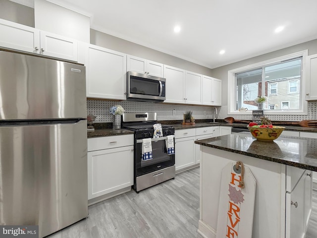1180 Cleveland St, Baltimore, MD 21230 - kitchen featuring stainless steel appliances, white cabinets, light wood-style floors, decorative backsplash, and dark stone countertops