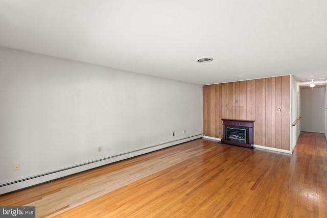 412 Fairview Ave, Winchester, VA 22601 - unfurnished living room featuring a baseboard radiator, wood finished floors, a glass covered fireplace, wood walls, and attic access