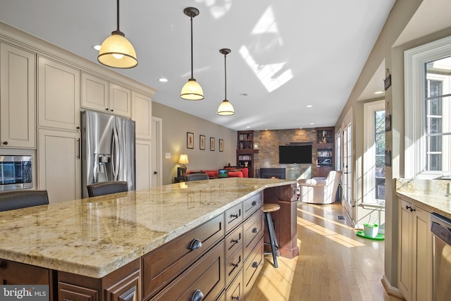 11603 Auburn Grove Ct, Reston, VA 20194 - kitchen featuring appliances with stainless steel finishes, cream cabinetry, a fireplace, light wood-type flooring, and light stone countertops