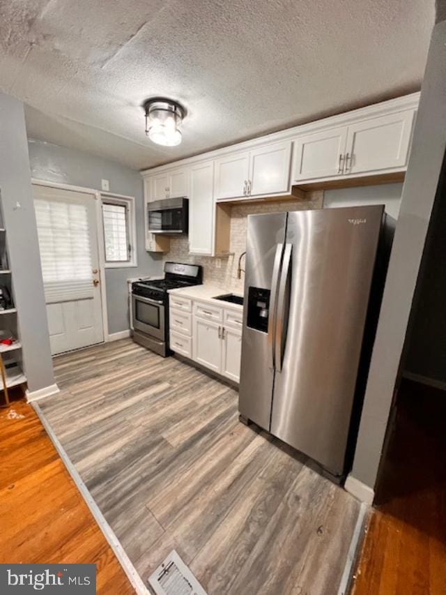 5904 Willet Ave, Baltimore, MD 21206 - kitchen featuring stainless steel appliances, white cabinets, light wood-style flooring, light countertops, and backsplash