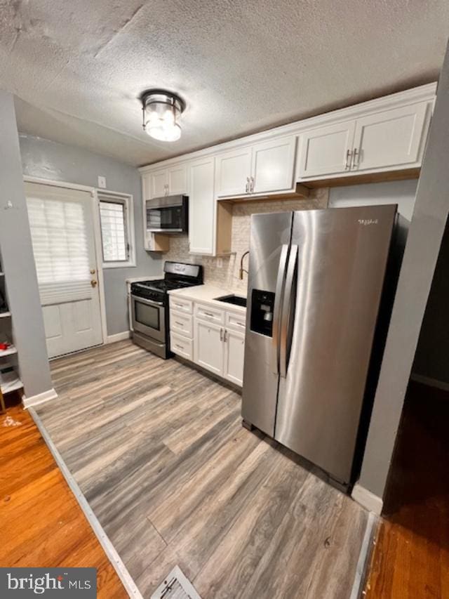 5904 Willet Ave, Baltimore, MD 21206 - kitchen featuring stainless steel appliances, white cabinets, light wood-style floors, light countertops, and a textured ceiling