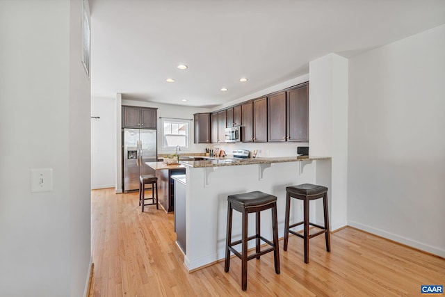 1254 Haden Pl, Crozet, VA 22932 - kitchen with stainless steel appliances, dark brown cabinetry, light stone counters, a breakfast bar area, and light wood-style flooring