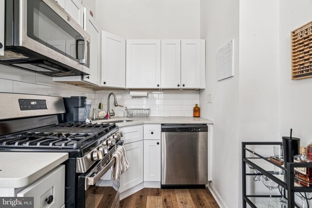 1917 Spring Garden St, Philadelphia, PA 19130 - kitchen featuring appliances with stainless steel finishes, light countertops, white cabinetry, dark wood-type flooring, and backsplash