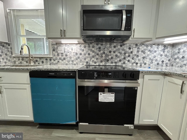 36697 W Club House Rd, Ocean View, DE 19970 - kitchen with stainless steel appliances, backsplash, wood finished floors, light stone counters, and white cabinetry