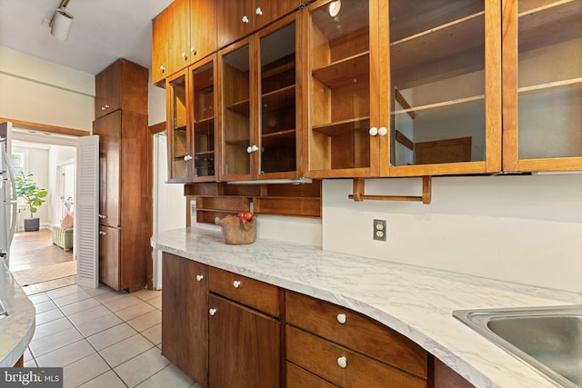 1623 Lanier Pl NW Unit 202, Washington, DC 20009 - kitchen featuring light tile patterned floors, glass insert cabinets, light stone counters, and brown cabinetry