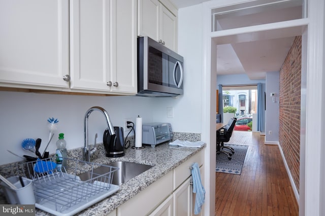 3238 P St NW, Washington, DC 20007 - kitchen featuring stainless steel microwave, white cabinetry, hardwood / wood-style floors, brick wall, and light stone countertops