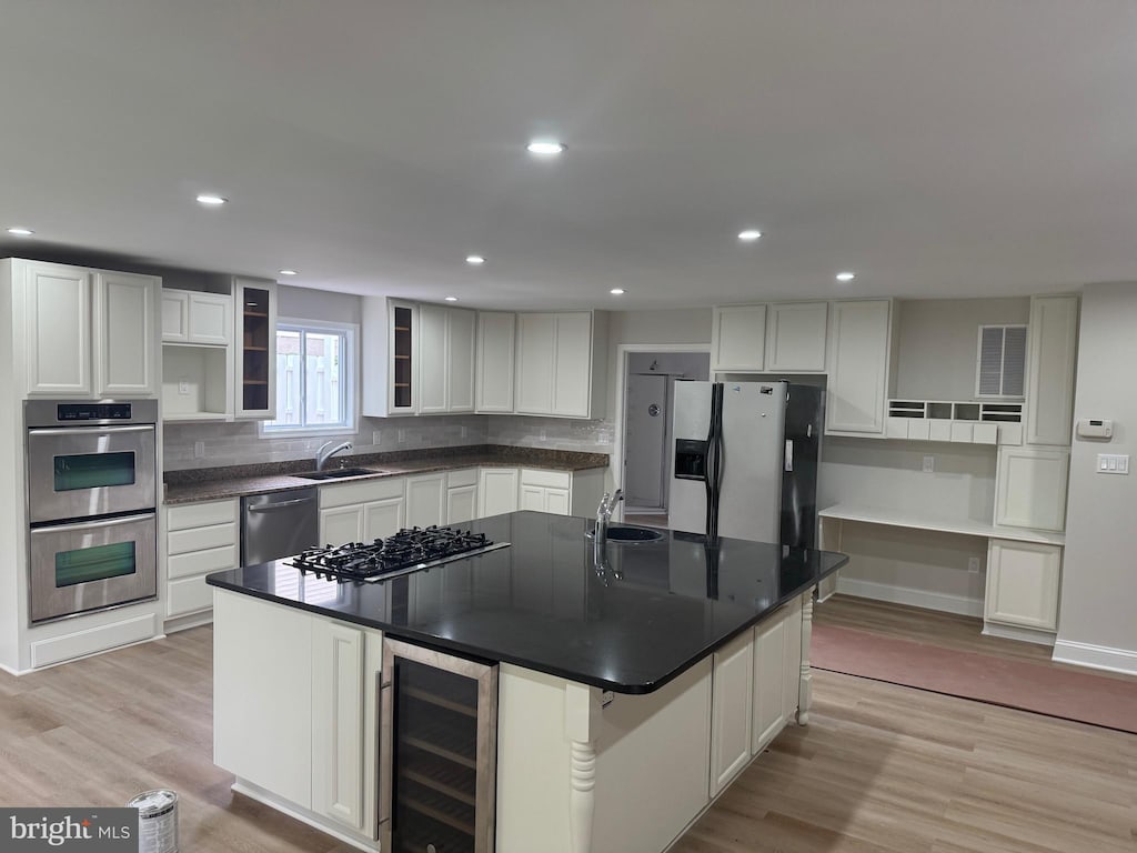 10408 Carlyn Ridge Rd, Damascus, MD 20872 - kitchen with wine cooler, stainless steel appliances, a kitchen island with sink, dark countertops, and light wood finished floors