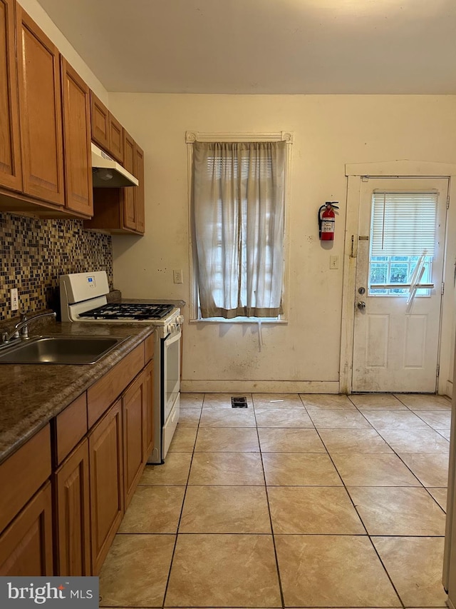 319 Bergen St, Gloucester City, NJ 08030 - kitchen with gas range gas stove, under cabinet range hood, brown cabinetry, decorative backsplash, and dark countertops