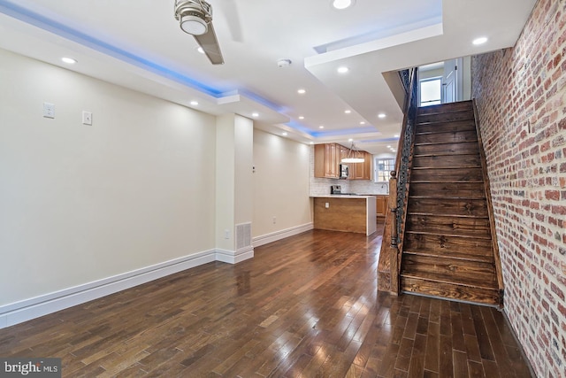 244 N Rose St, Baltimore, MD 21224 - unfurnished living room featuring a raised ceiling, brick wall, dark wood-style flooring, stairway, and recessed lighting