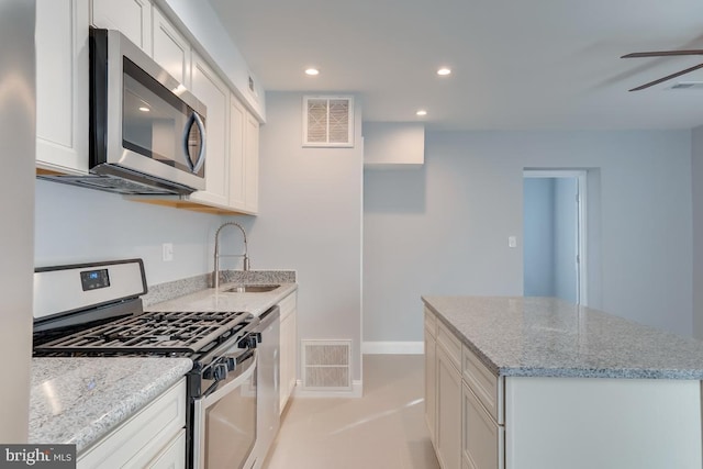 537 Newcomb St SE, Washington, DC 20032 - kitchen featuring stainless steel appliances, white cabinets, light stone counters, a ceiling fan, and a center island