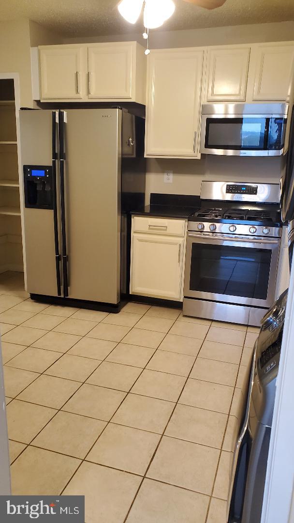 3705 S George Mason Dr Unit 1311, Falls Church, VA 22041 - kitchen featuring stainless steel appliances, white cabinets, dark countertops, and light tile patterned floors