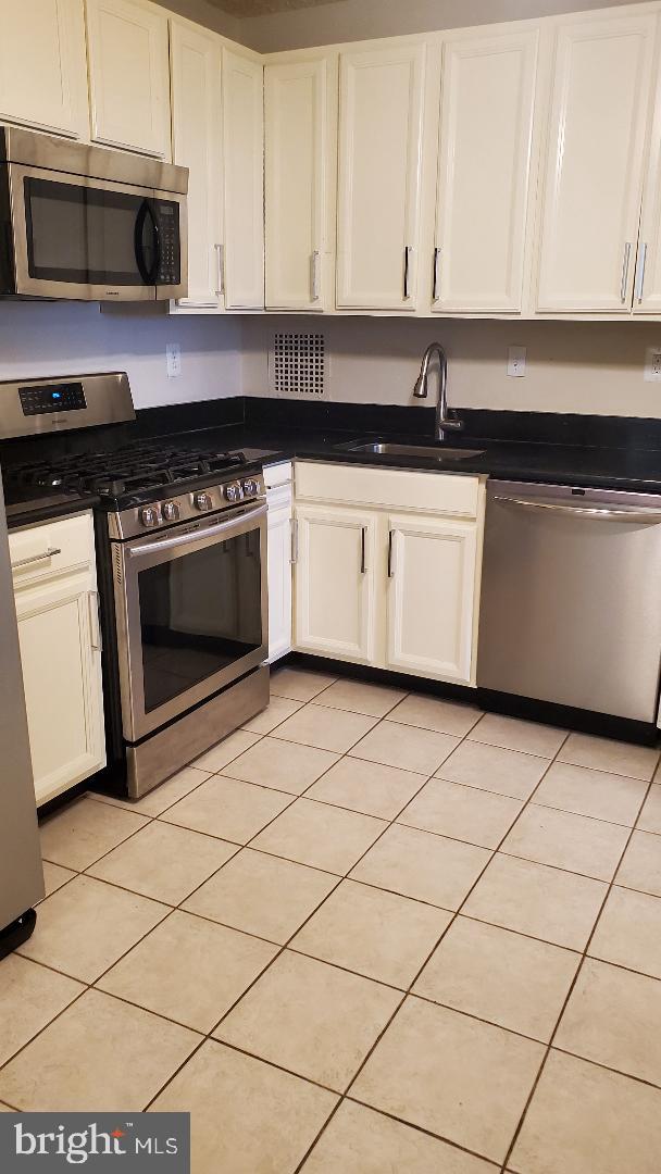 3705 S George Mason Dr Unit 1311, Falls Church, VA 22041 - kitchen featuring appliances with stainless steel finishes, dark countertops, white cabinetry, and light tile patterned flooring