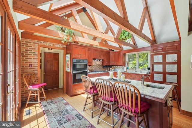 4250 Fretz Mill Rd, New Hope, PA 18938 - kitchen featuring light wood-type flooring, high vaulted ceiling, light stone counters, an island with sink, and brown cabinets
