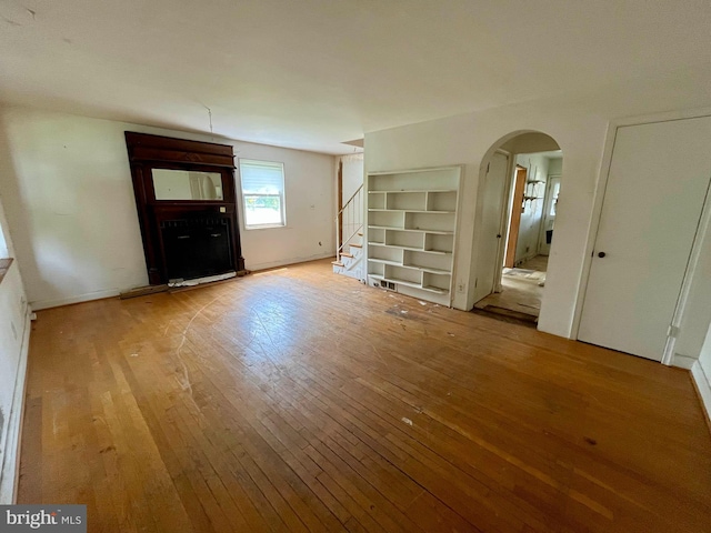 5501 W Forest Park Ave, Baltimore, MD 21207 - unfurnished living room with wood-type flooring, arched walkways, and stairway