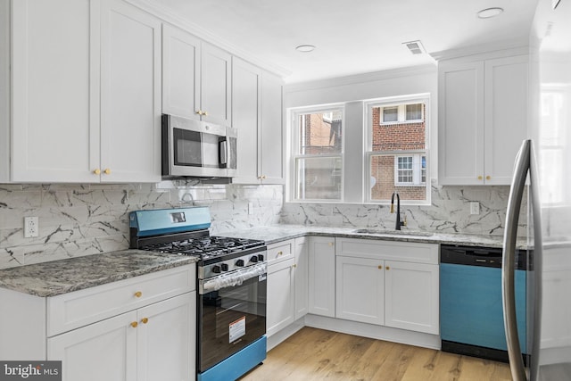 913 E Sanger St, Philadelphia, PA 19124 - kitchen featuring appliances with stainless steel finishes, white cabinetry, ornamental molding, light wood finished floors, and backsplash