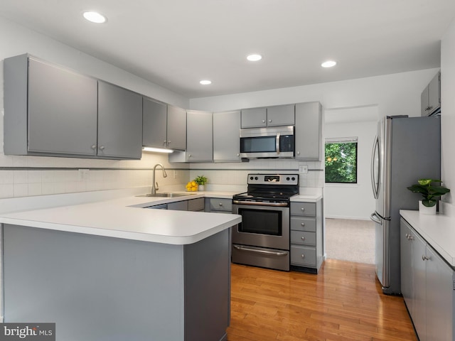 398 Lynetree Dr Unit 11-D, West Chester, PA 19380 - kitchen with stainless steel appliances, gray cabinetry, a peninsula, light wood-style flooring, and backsplash