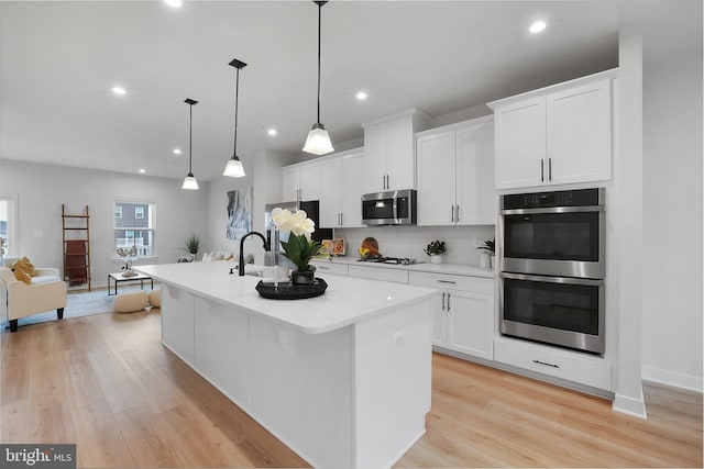 8109 Primrose Ln, Laurel, MD 20723 - kitchen featuring stainless steel appliances, a center island with sink, tasteful backsplash, light wood-type flooring, and light countertops