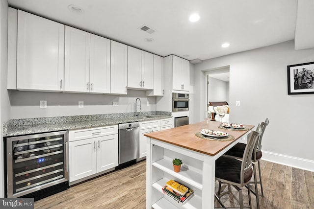 3831 Fulton St NW, Washington, DC 20007 - kitchen featuring beverage cooler, appliances with stainless steel finishes, light wood finished floors, white cabinets, and a breakfast bar